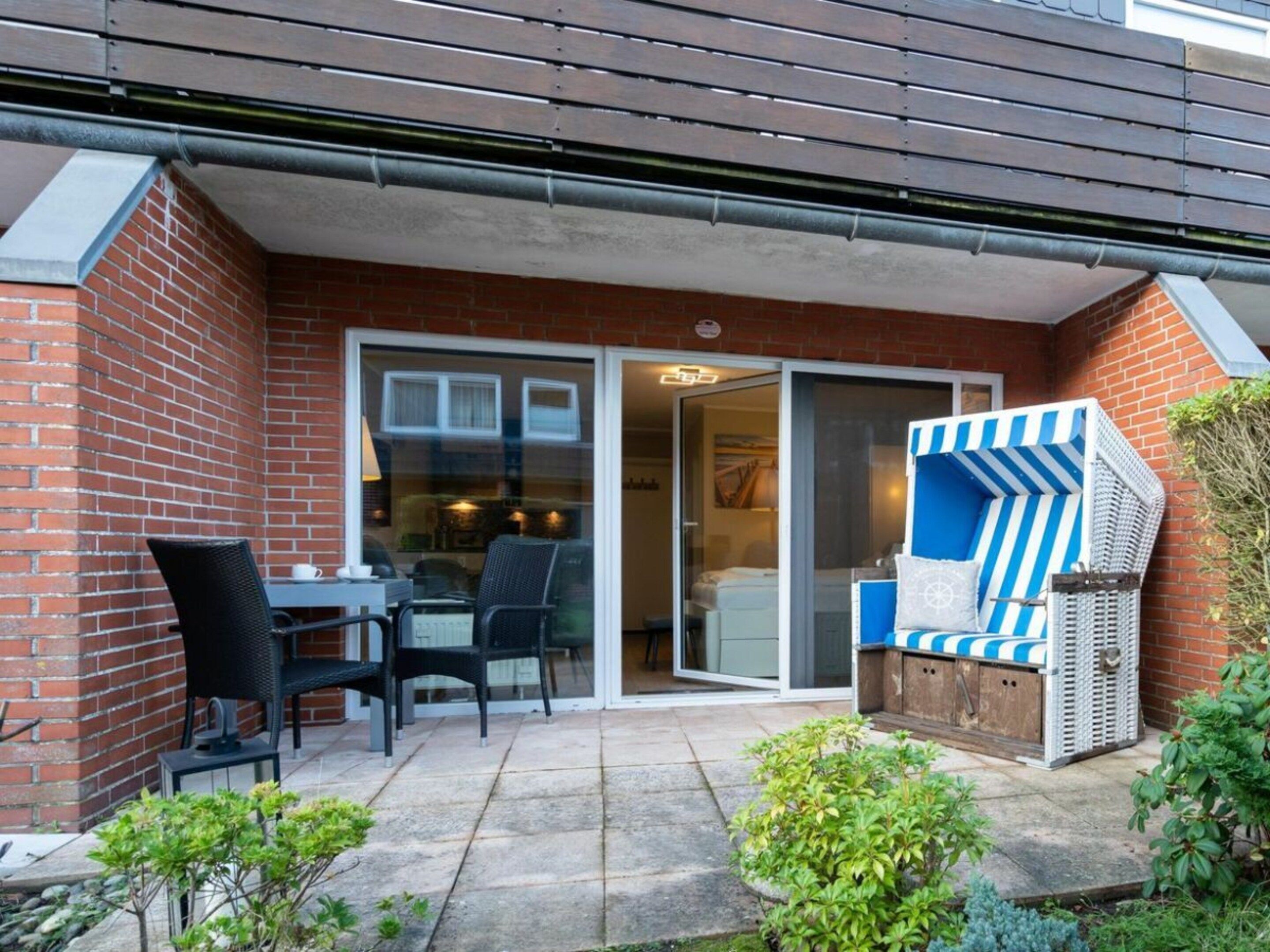 A brick exterior with a sliding glass door leading to a patio area with a table, chairs, and a wicker sofa.
