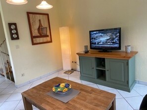 Un salon avec une table basse en bois, un téléviseur posé sur un meuble, un tableau accroché au mur et un escalier en arrière-plan.