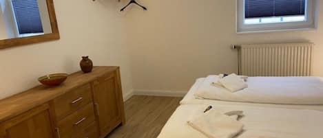 A bedroom with two beds, a wooden dresser, a mirror, a radiator, and a window with blinds.
