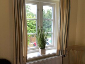 Une fenêtre donnant sur un espace verdoyant, un radiateur en dessous et une chaise sur la droite.