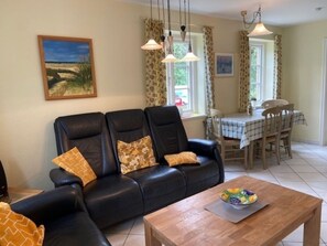 Un salon avec un canapé en cuir noir, une table basse en bois et un coin repas comprenant une table et des chaises.