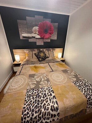 Quarto com cama, duas luminárias de cabeceira, cabeceira com desenho floral e quadro pendurado na parede.