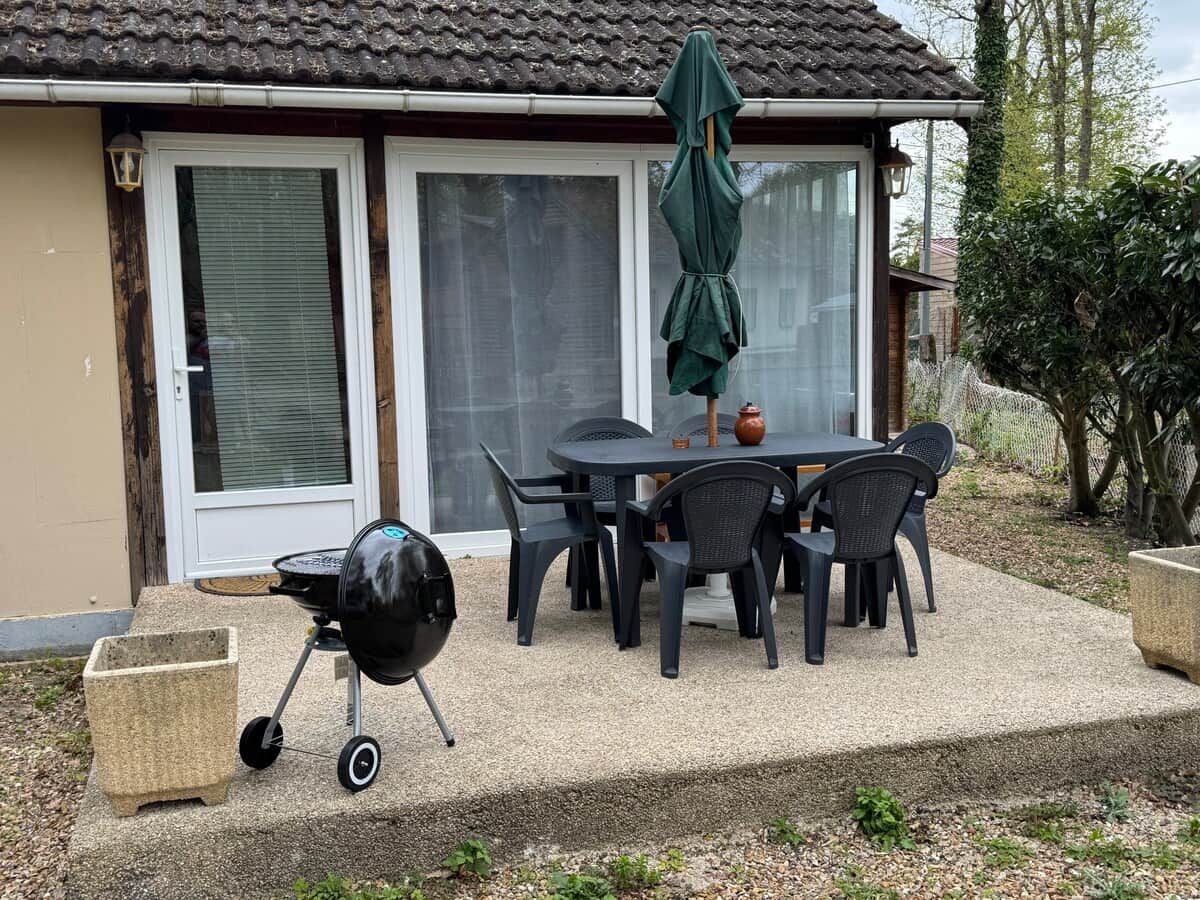 An outdoor patio with a grill, table, chairs, and a covered umbrella.