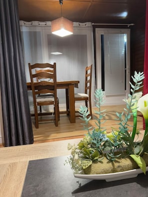 Uma área de refeições com mesa e cadeiras de madeira, luminária pendente e planta em vaso com flores artificiais.