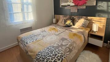 Een slaapkamer met een bed, nachtkastje, kunstwerk aan de muur en een raam met dunne gordijnen.