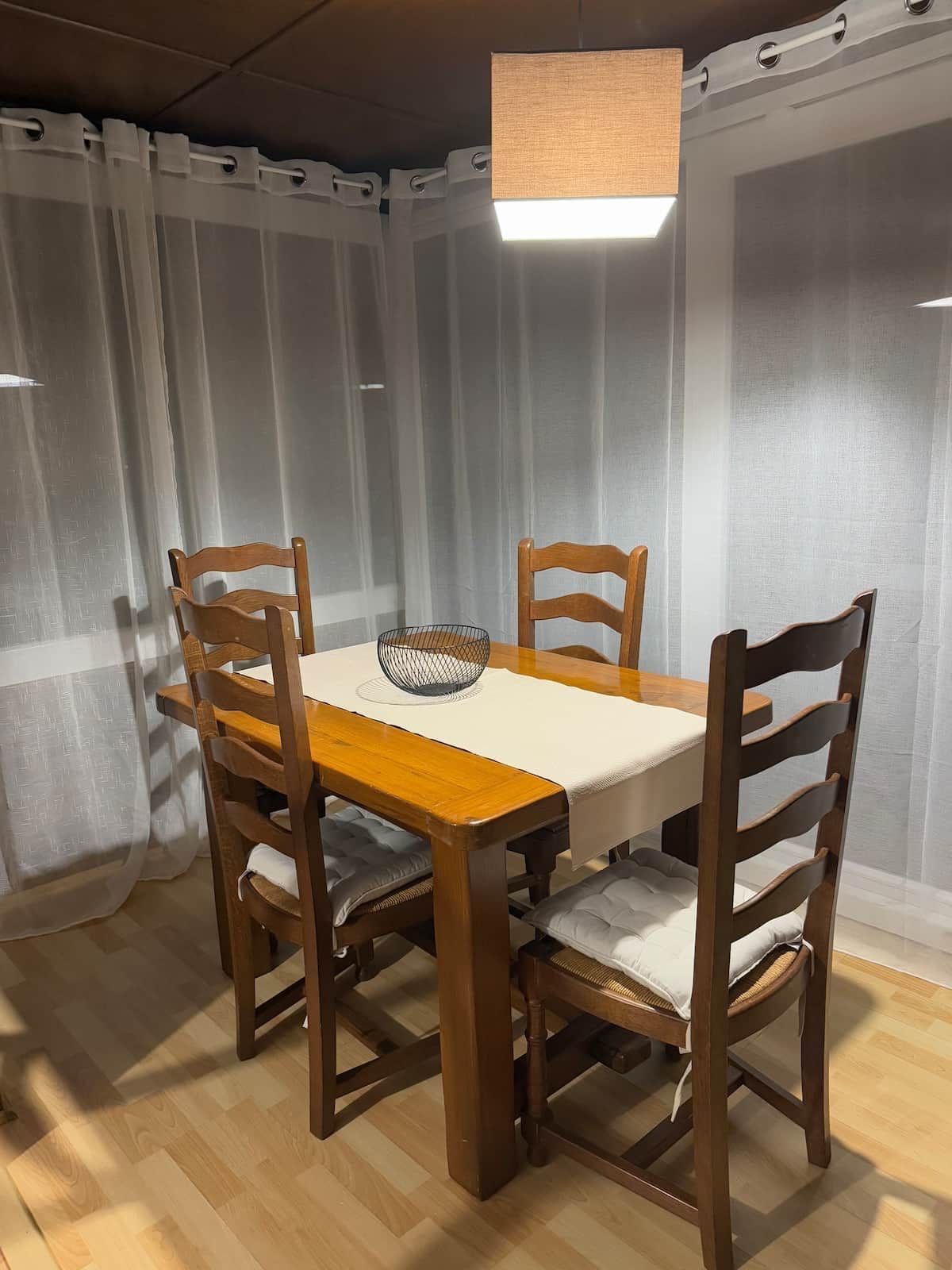 A dining area with a wooden table, four chairs, and a hanging light fixture.