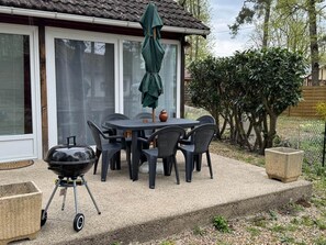 Une terrasse extérieure avec une table et des chaises, un barbecue et un parasol.