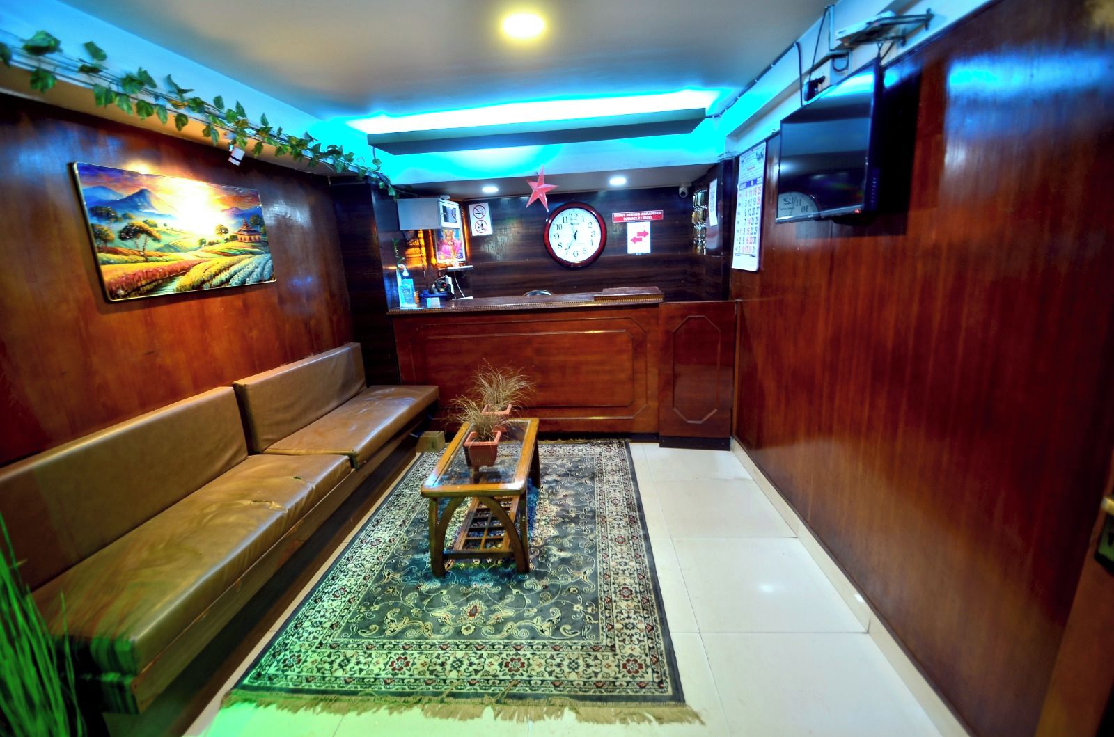 A room with a wooden bench, a small table with a plant, a clock, and a wall-mounted TV.