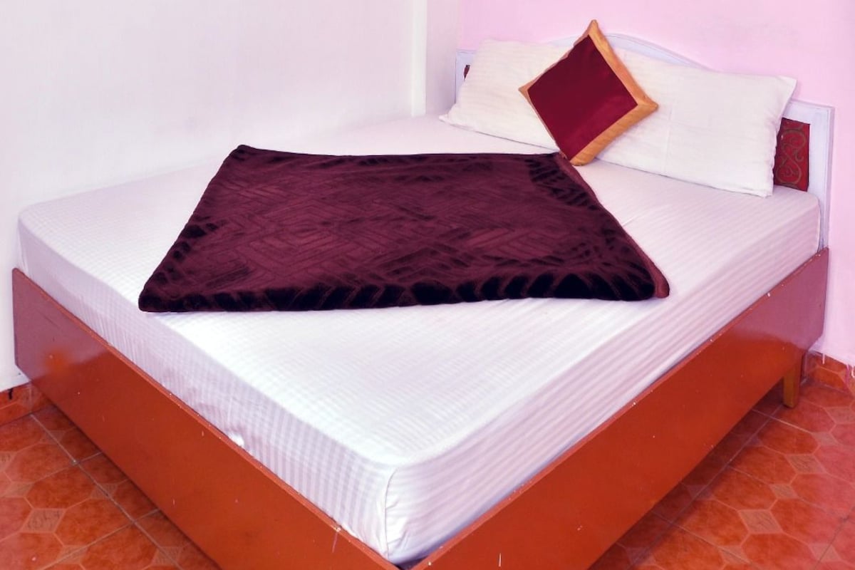 Een eenpersoonskamer met een wit matras, een donkerbruine deken en twee kussens.