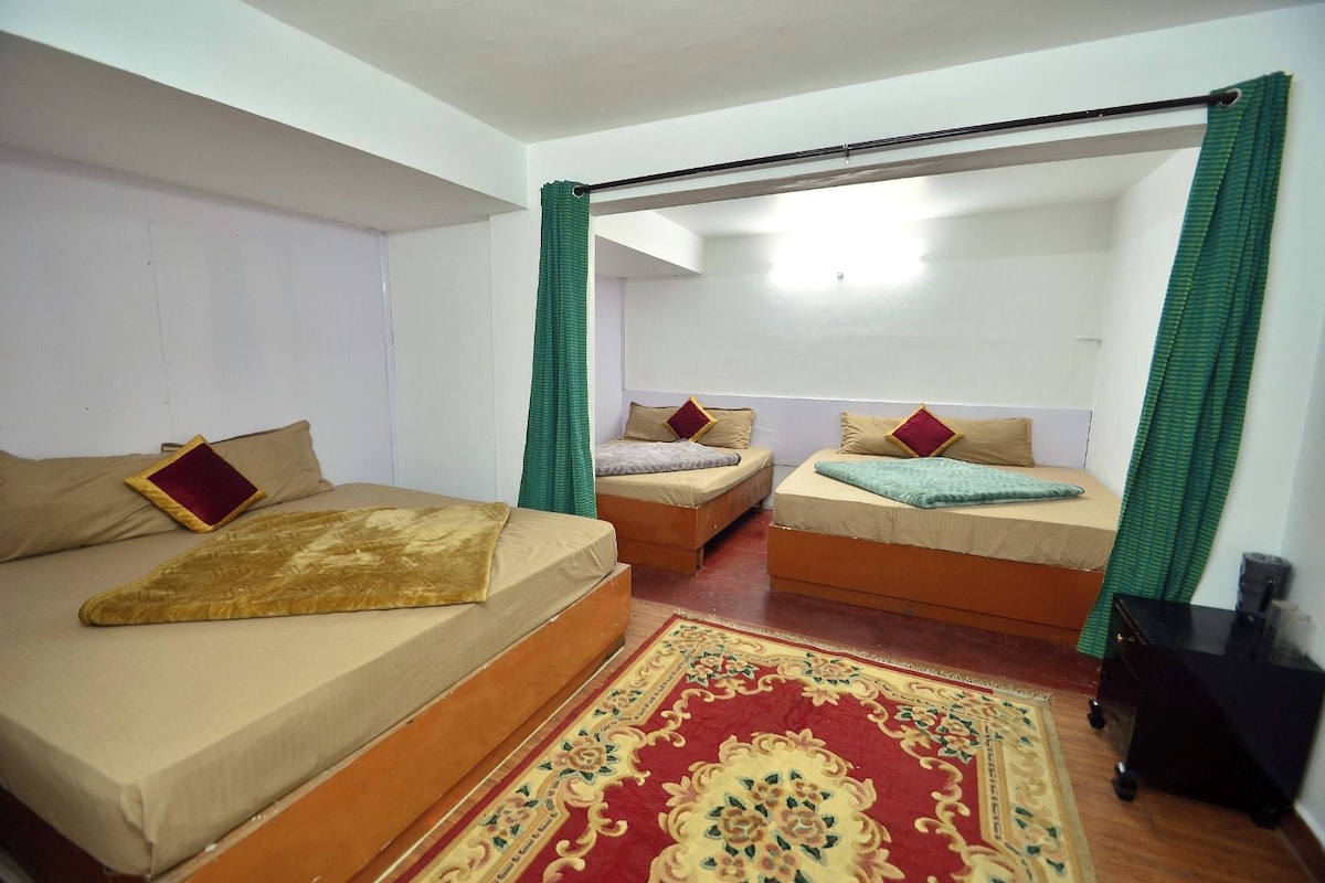 Een kamer met twee bedden, een rood tapijt met patroon en een zwart nachtkastje.