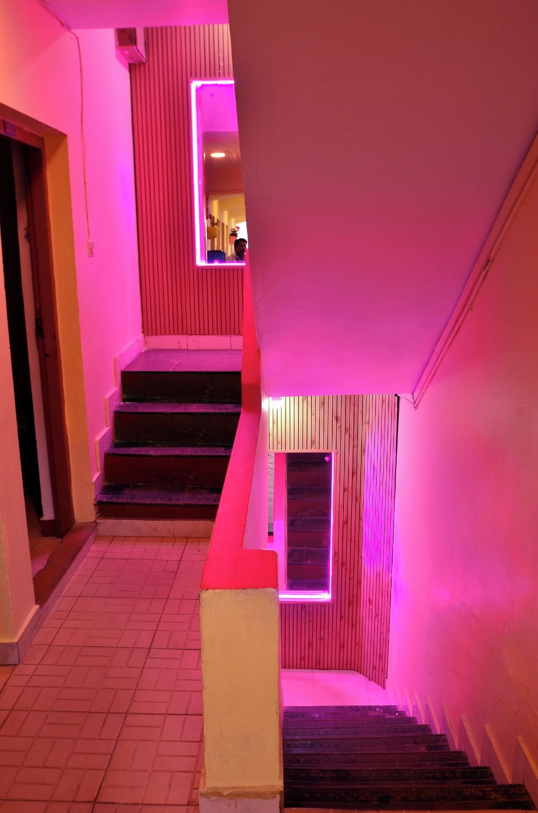 A staircase with a pink-lit wall and a door at the top.