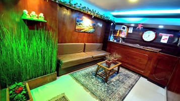 A room with a sofa, a small table with plants, a decorative wall, and a clock.