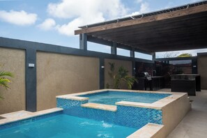 Ein Swimmingpool mit gefliestem Rand, ein Grillplatz und eine überdachte Terrasse.