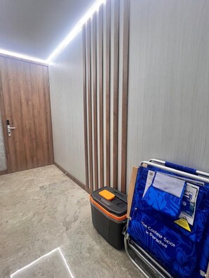 A hotel room with a wooden door, a vertical wooden panel wall, a tiled floor, a suitcase, and a cart with a blue bag. - New Listing (San Nicolas)