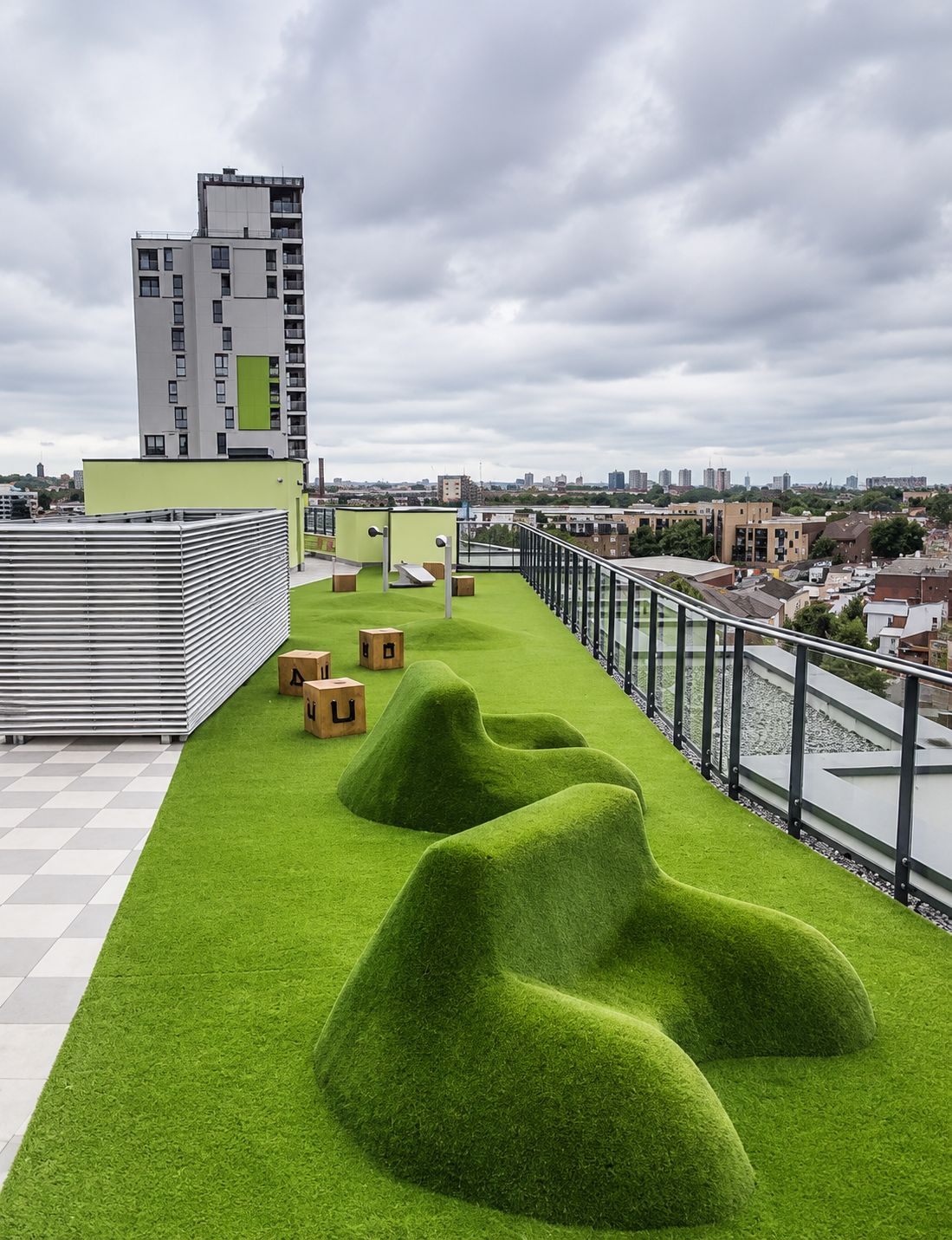 A rooftop terrace with artificial grass, seating areas, and a view of the cityscape.