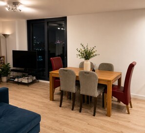 A dining area with a wooden table and chairs, a television on a stand, and a city view through a large window. - Amazing apartment near London Bridge, Tower Brigdge and City of London (London)