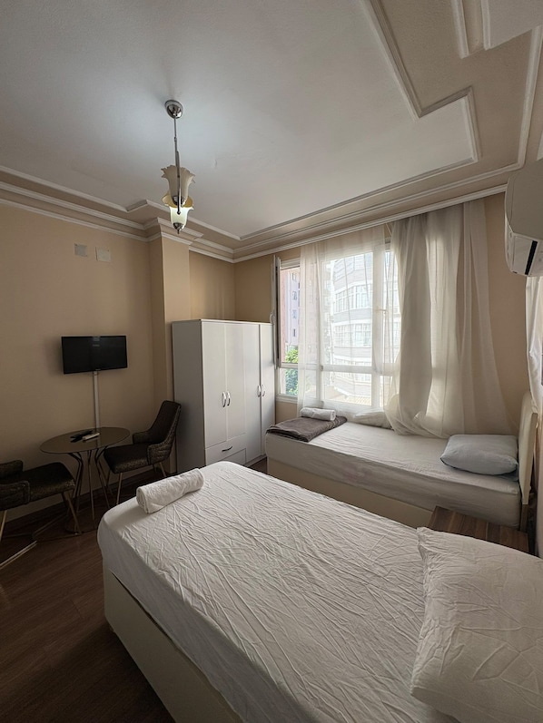 Une chambre d’hôtel avec deux lits, un bureau avec une chaise, une télévision et une armoire.