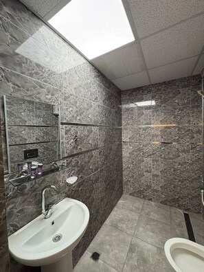 Ein modernes Badezimmer mit Marmorwand, Waschbecken, Spiegel und Duschbereich.