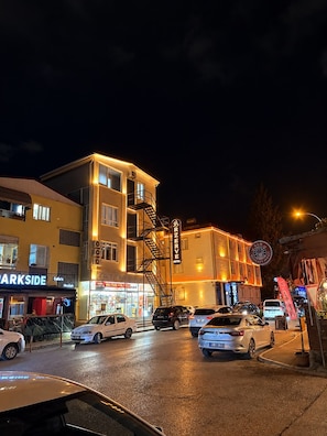 Ein mehrstöckiges Hotel mit Feuerleiter, einem sichtbaren Restaurant namens 'Café's Hookah' und einem Parkplatz mit mehreren Autos.