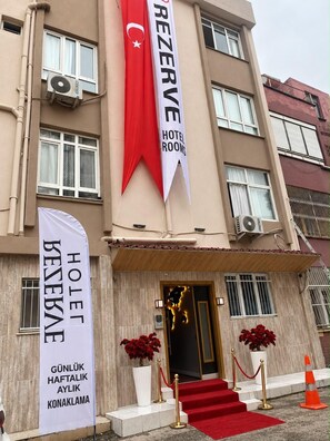 Ein Hotel Eingangsbereich mit rotem Teppich, einer Flagge und einem Banner, das 'HOTEL ROOMS' anzeigt.