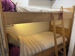 Een stapelbed met een ladder, een enkel bed eronder en een wandplank.
