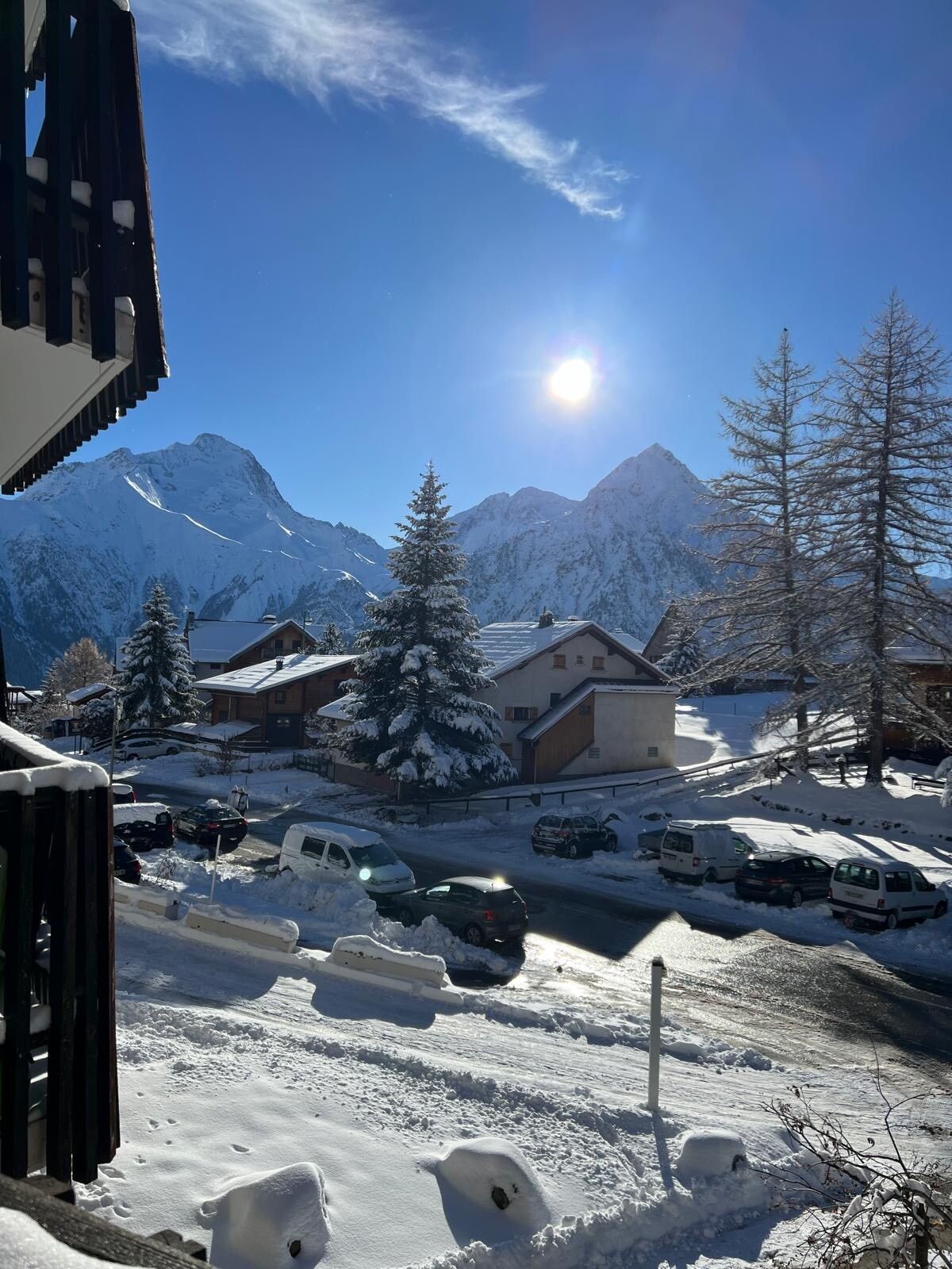 A snowy mountain village with buildings, parked cars, and a clear sky.