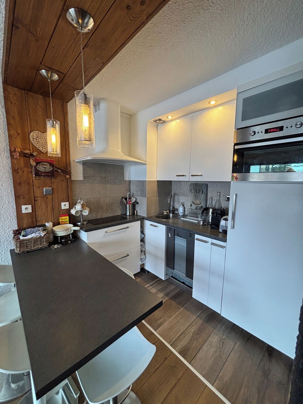 Una cocina moderna con una isla central, armarios blancos, electrodomésticos de acero inoxidable e iluminación colgante.