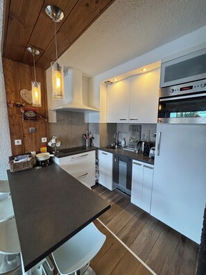 A modern kitchen with a central island, white cabinetry, stainless steel appliances, and pendant lighting. - Appartement cosy – aux 2 Alpes (Les Deux Alpes)