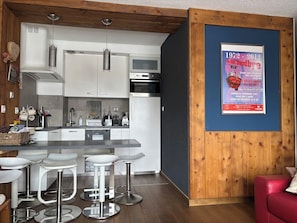 A modern kitchen with white cabinets, stainless steel appliances, and a bar area with white stools. - Appartement cosy – aux 2 Alpes (Les Deux Alpes)