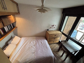 A bedroom with a bed, a wooden dresser, a window with a view, and a ceiling fan. - Appartement cosy – aux 2 Alpes (Les Deux Alpes)