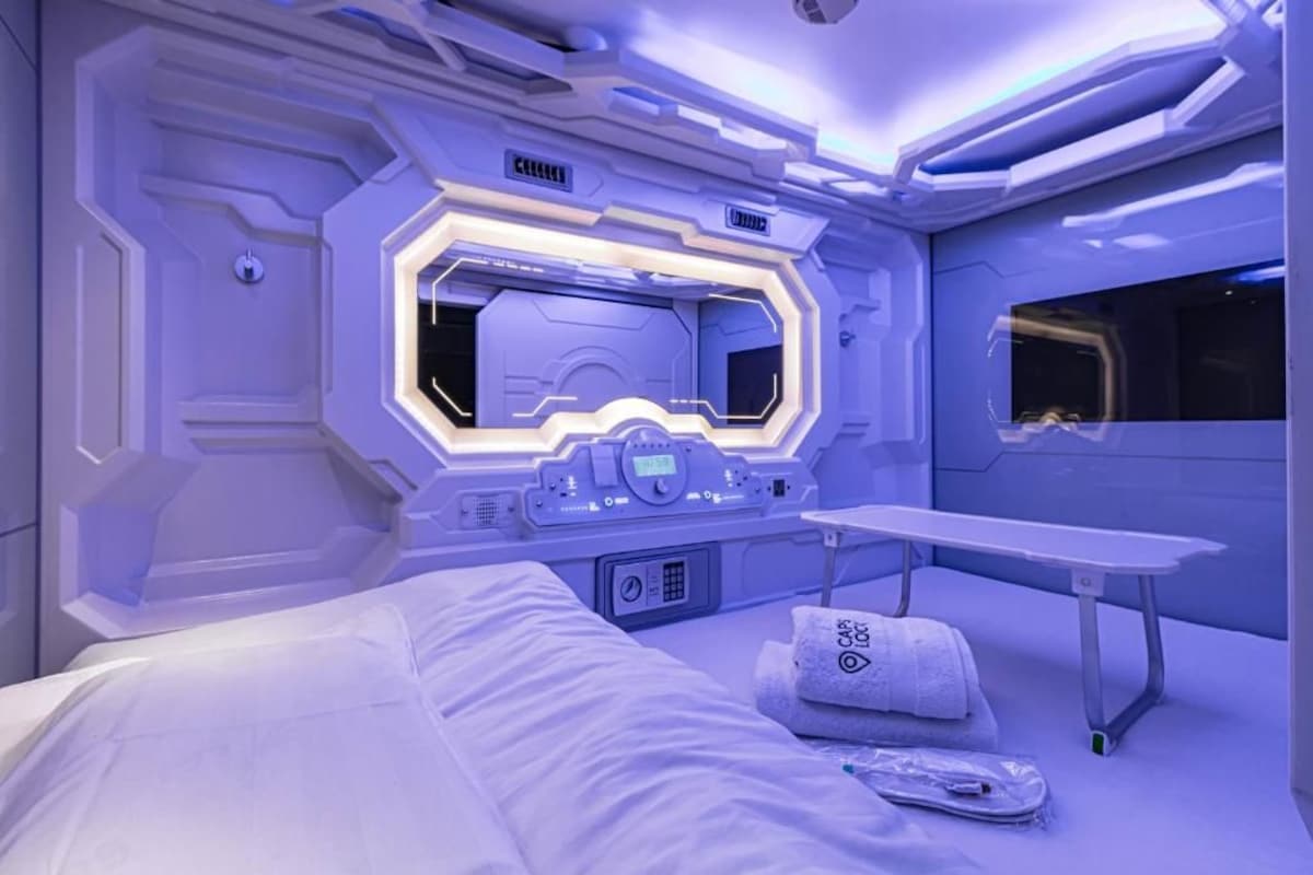 Ein futuristisches Zimmer mit einem Bett, einer Sitzbank und einem wandmontierten Bedienfeld.