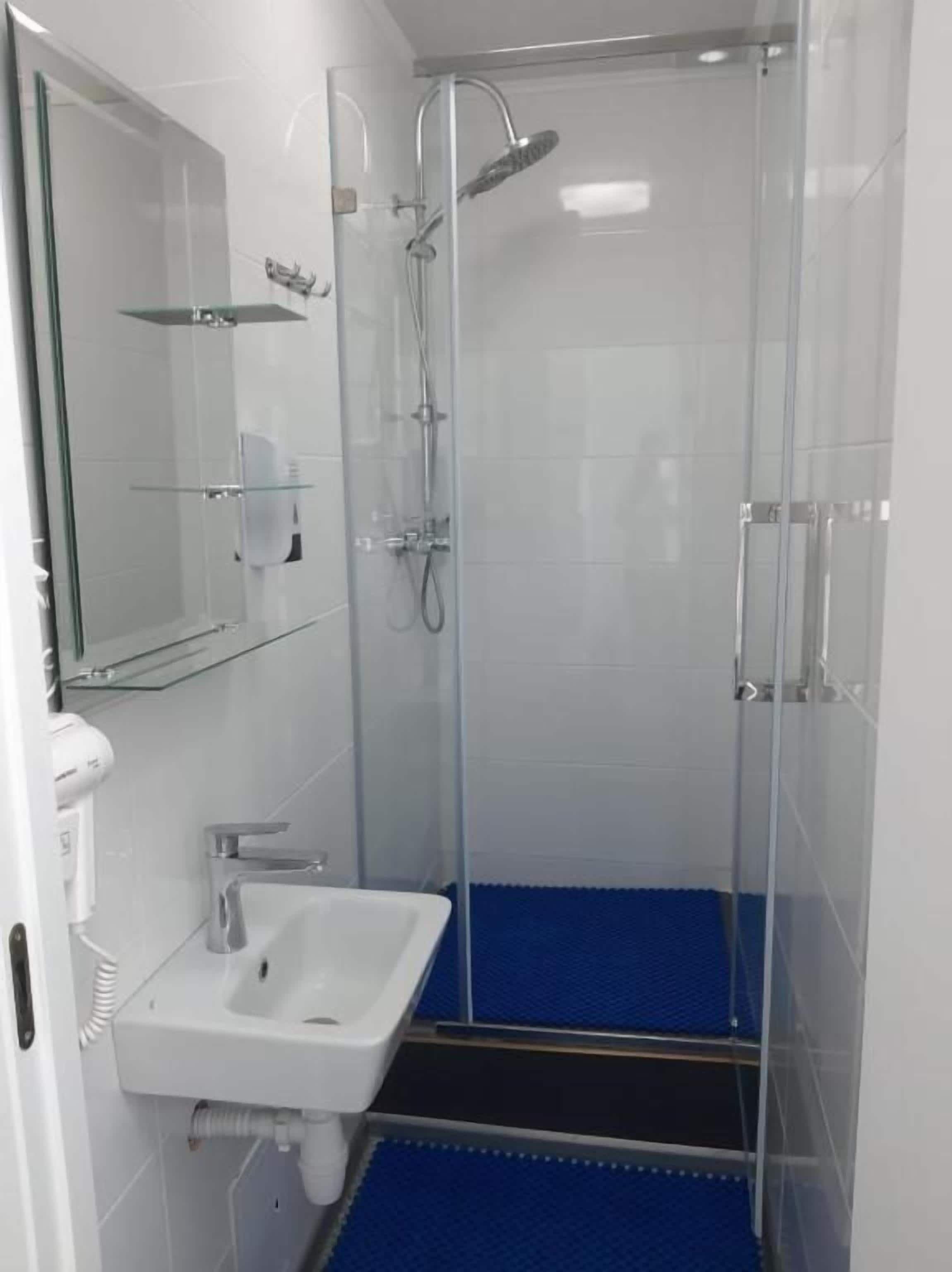 Un baño moderno con cabina de ducha de vidrio, un lavamanos blanco y una alfombra de ducha azul.