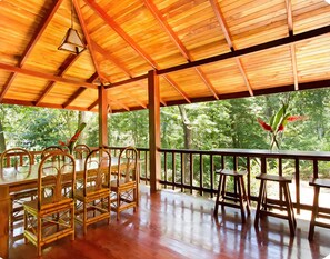Une terrasse extérieure en bois, agrémentée de tables et de chaises, et entourée d’une végétation luxuriante.