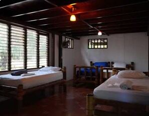 Ein Zimmer mit zwei Holzbetten, einem Ventilator und einem Fenster mit Gitterstäben.