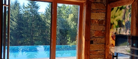 A room with a stone floor, wooden ceiling, and a large glass door leading to a swimming pool.