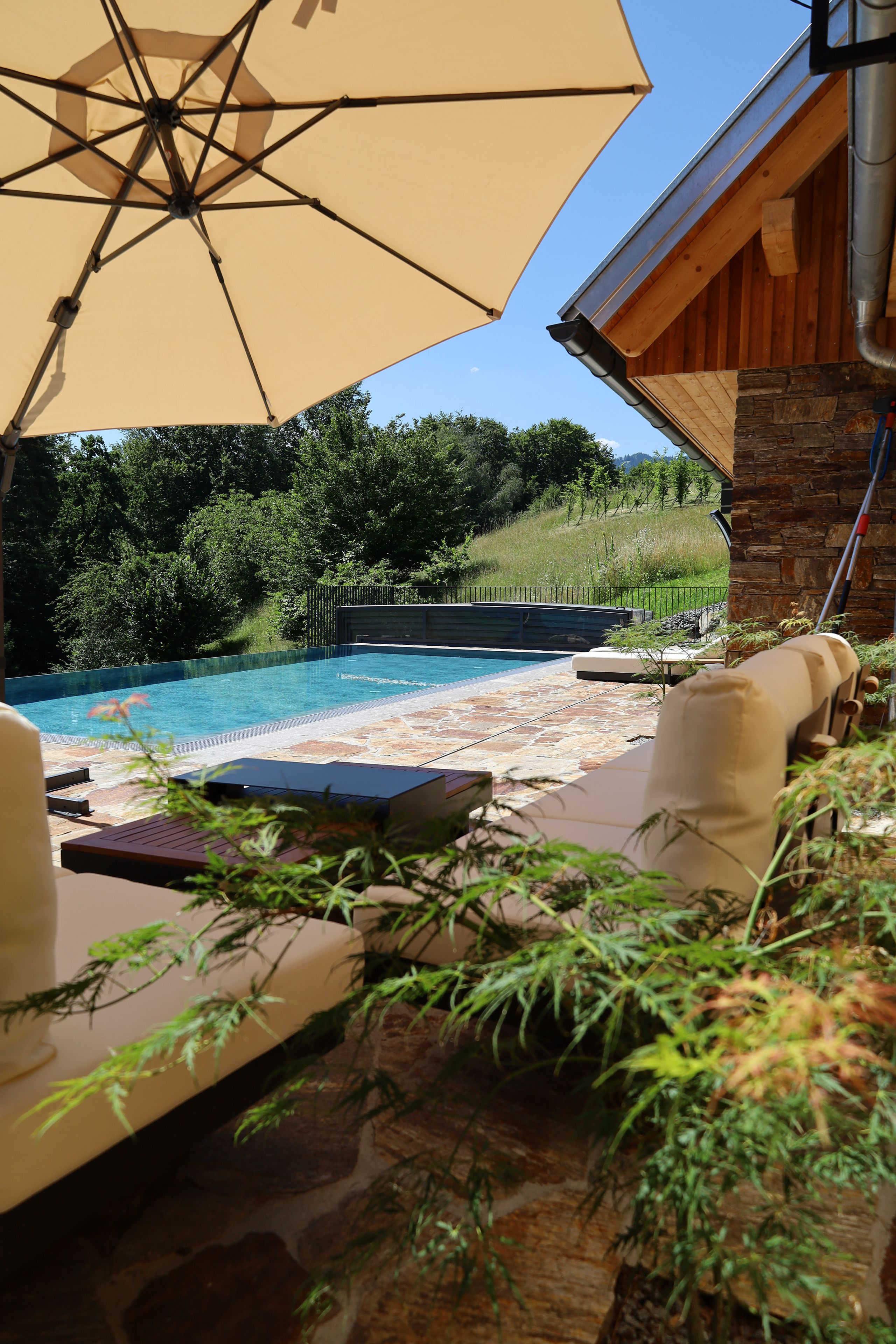 An outdoor pool area with a lounge chair, a table, and a large umbrella.