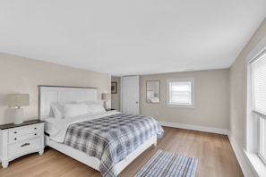 Quarto com cama, mesas de cabeceira, abajur, espelho e janela com persianas.