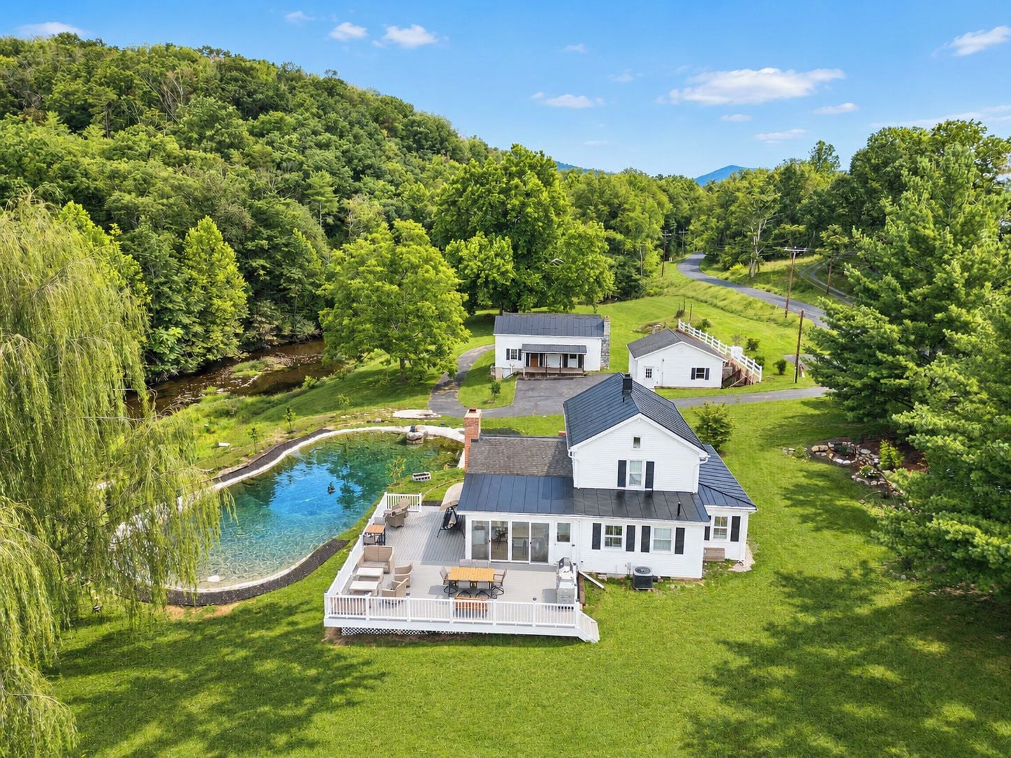 Une grande maison avec une piscine, entourée d’une végétation luxuriante et de collines.
