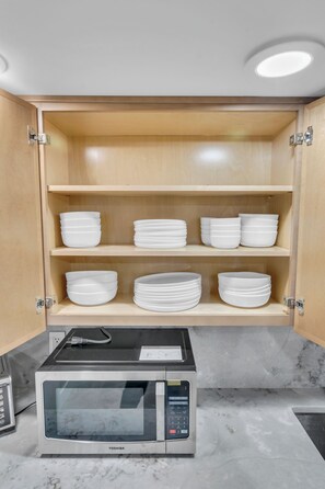 Una cocina con microondas y repisas con cuencos blancos.