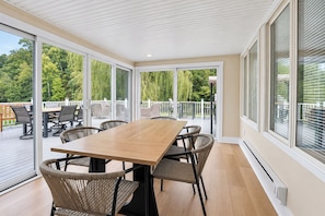 Um quarto espaçoso com uma mesa grande e cadeiras, janelas amplas e vista para um deck com móveis de exterior.
