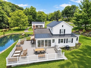 Ein zweistöckiges Haus mit einer Terrasse, einem Teich und einem Garten.
