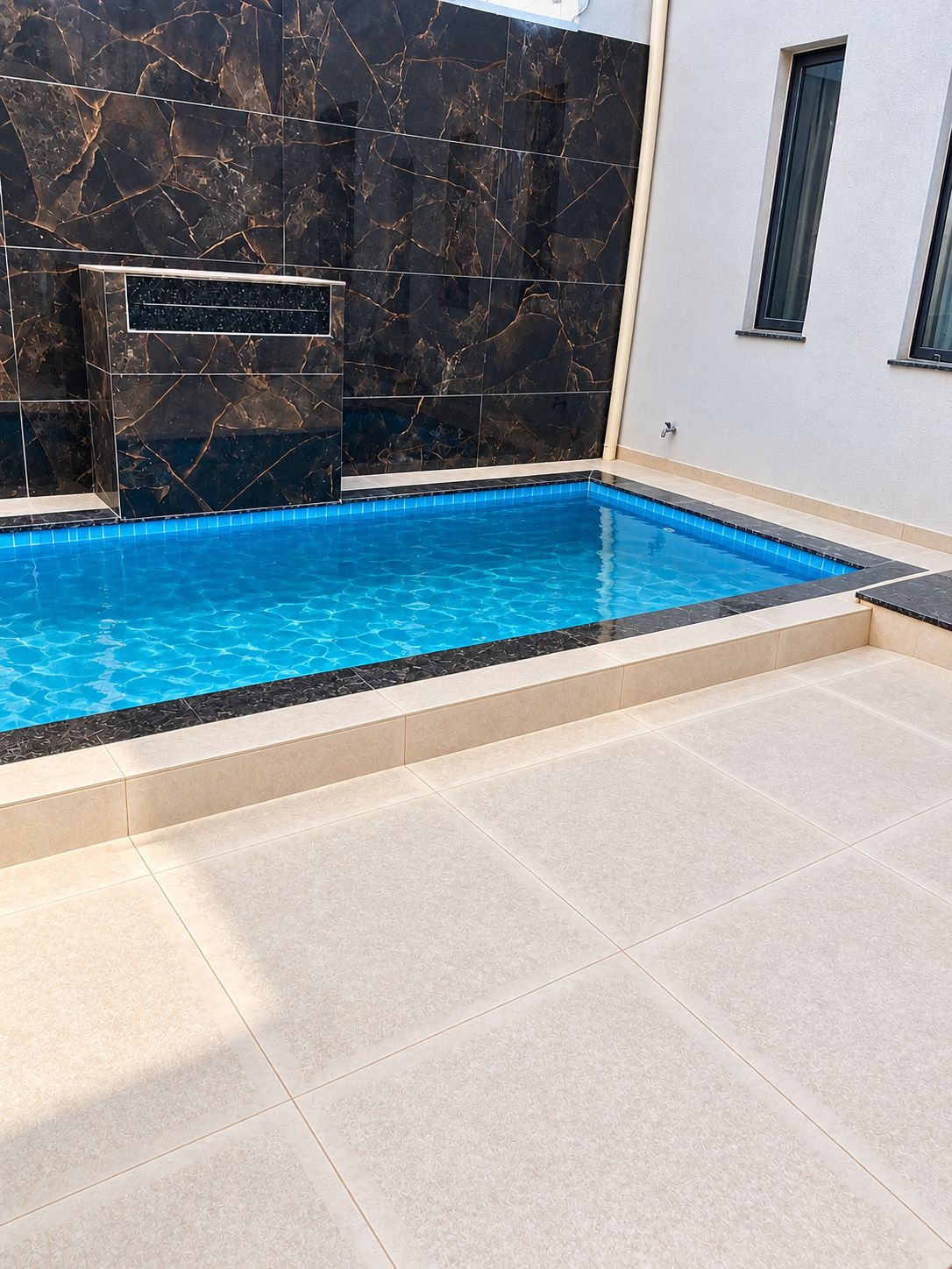 Una piscina rectangular con una pared de mármol negro y suelo de baldosas.