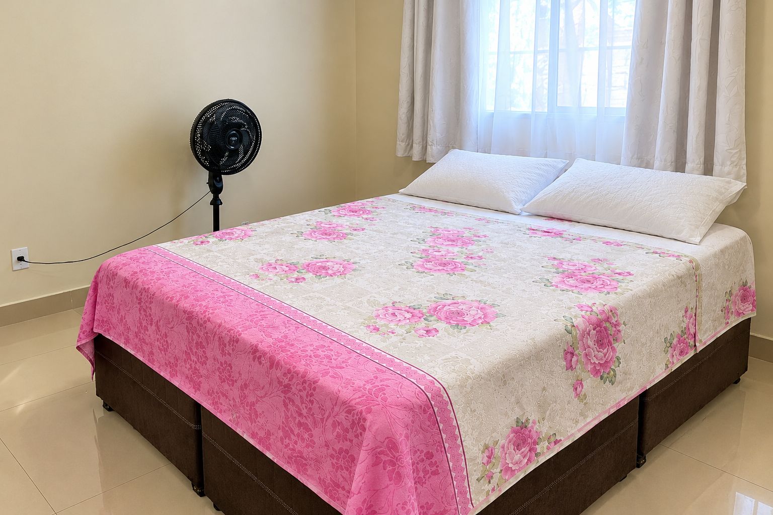 A bedroom with a bed, a standing fan, and a window with curtains.
