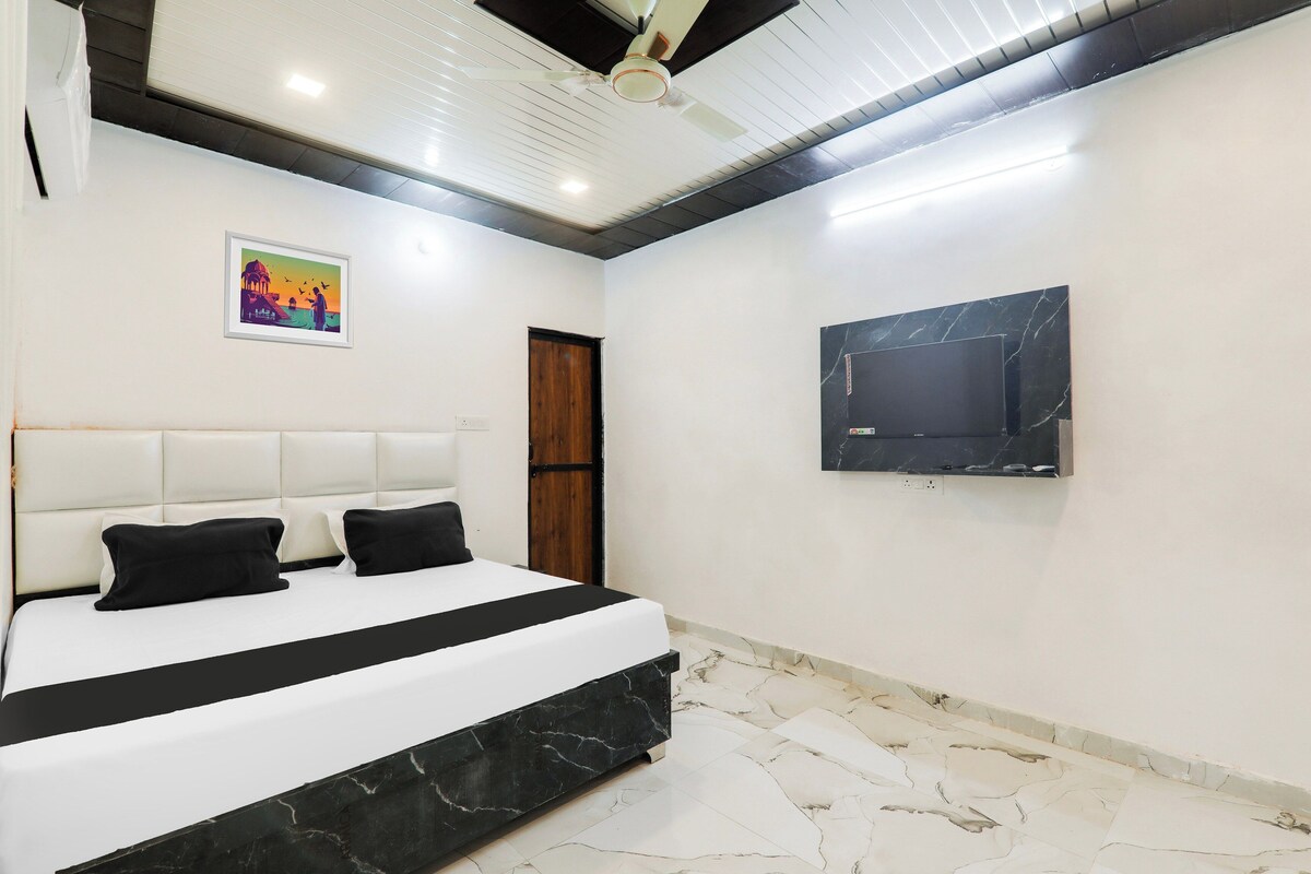 Un dormitorio con una cama, ventilador de techo, televisor montado en la pared y un cuadro enmarcado.