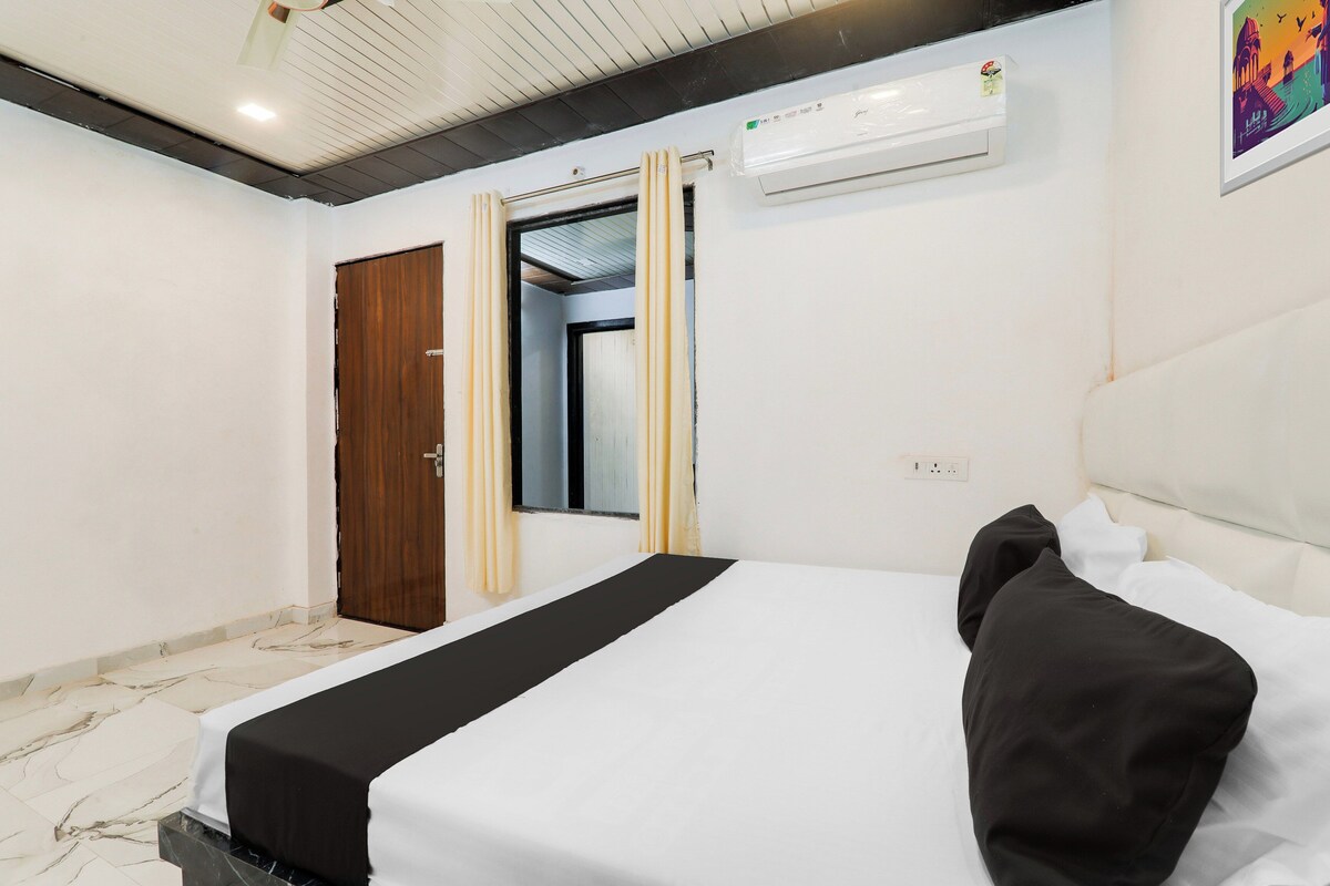 Habitación de hotel con cama, ventana con cortinas, unidad de aire acondicionado y una obra de arte colgada en la pared.