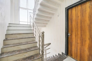 A staircase with marble steps and a metal handrail leading to a wooden door. - Hotel O S.S tower (Kanpur)