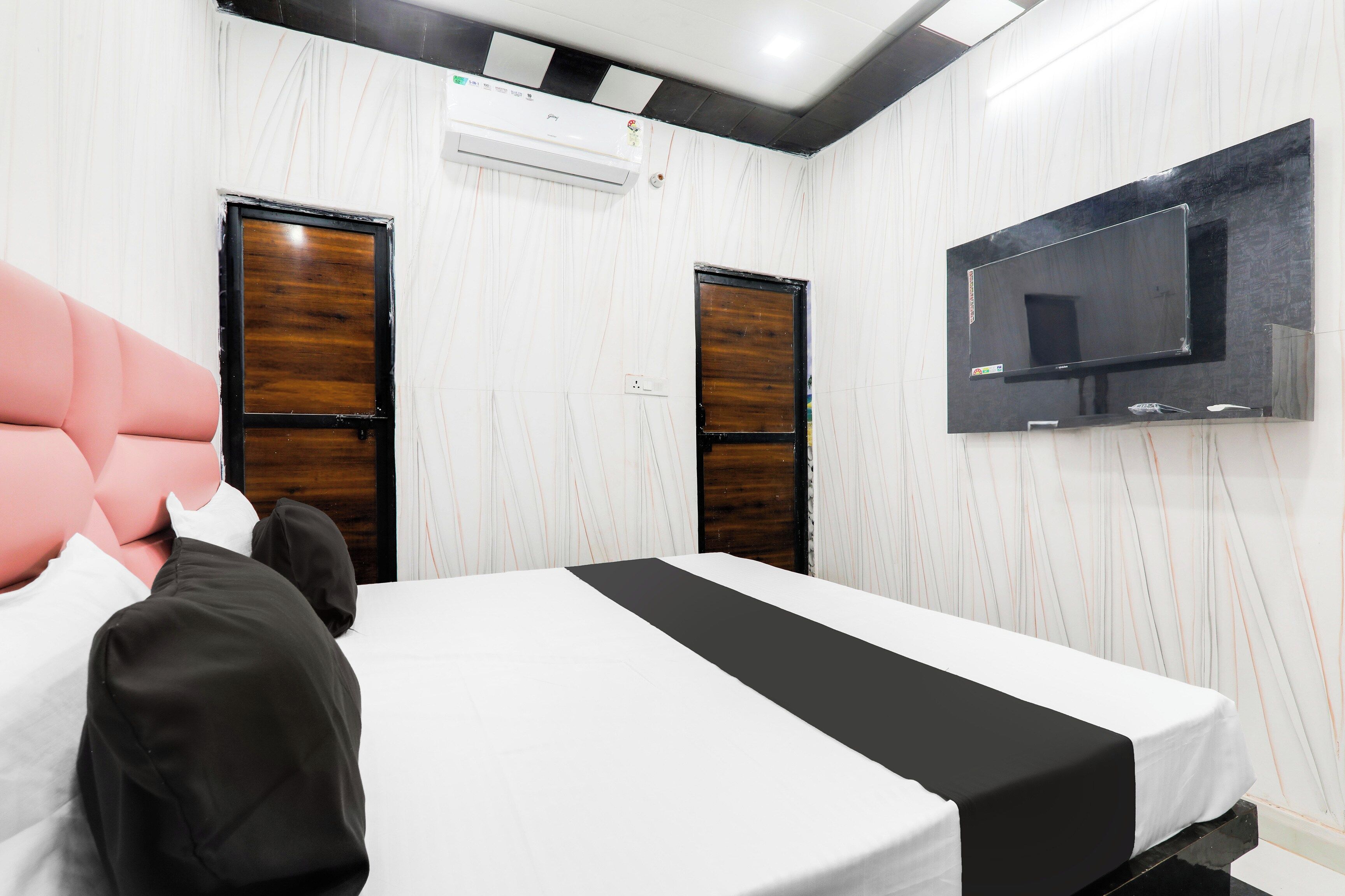 Quarto de hotel com uma cama, televisão na parede e duas portas.