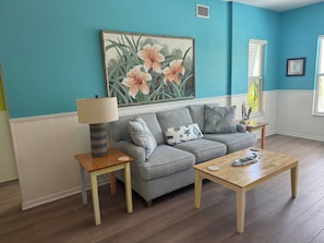 A living room with a grey sofa, a wooden coffee table, a lamp, and a painting of flowers on the wall. - Siesta Key | Pool, Spa & Flexible 1-2 Bedroom Lock-Off (Siesta Key)