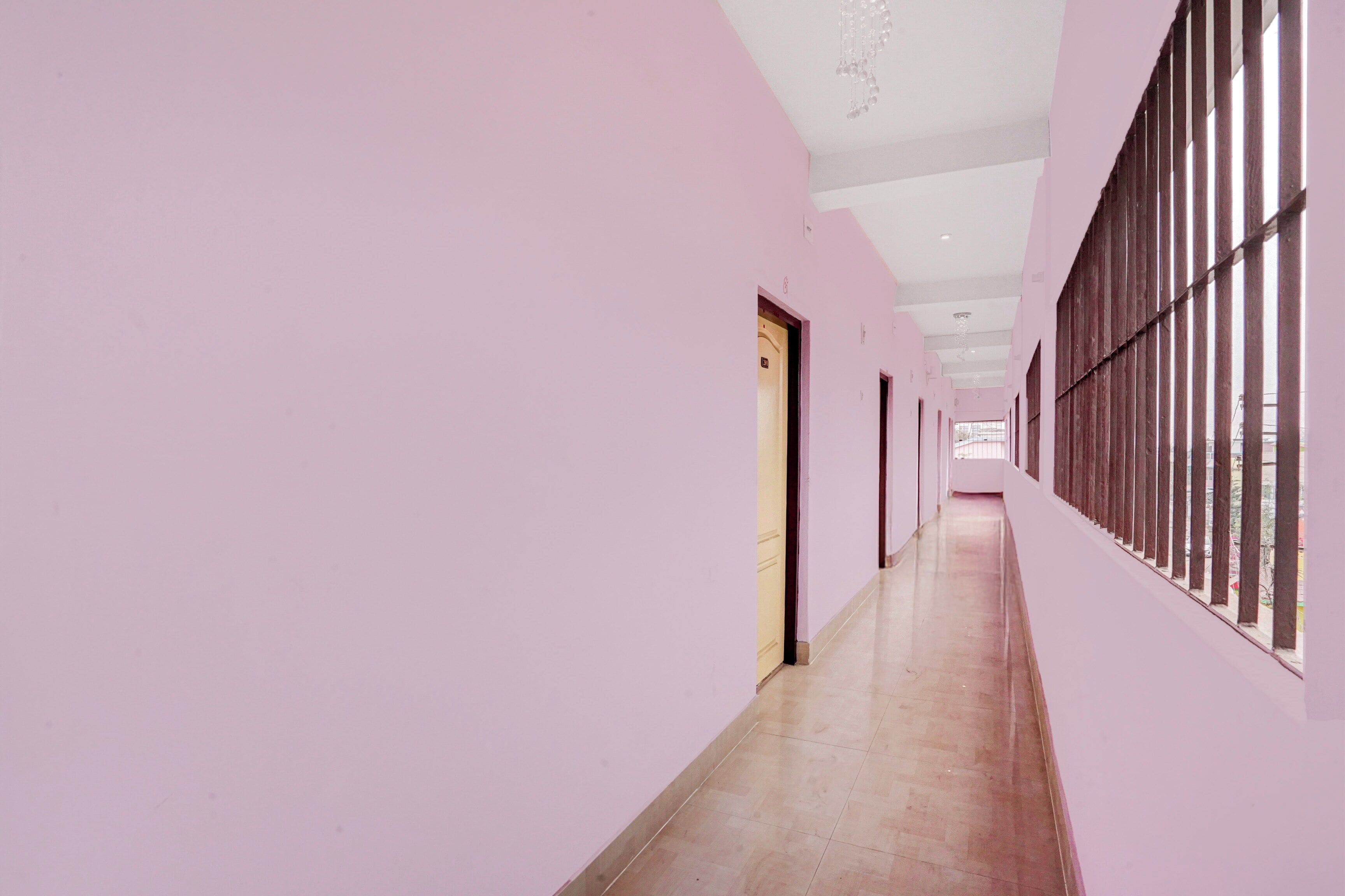 Un pasillo con paredes rosas y piso de madera, que conduce a una puerta al final.
