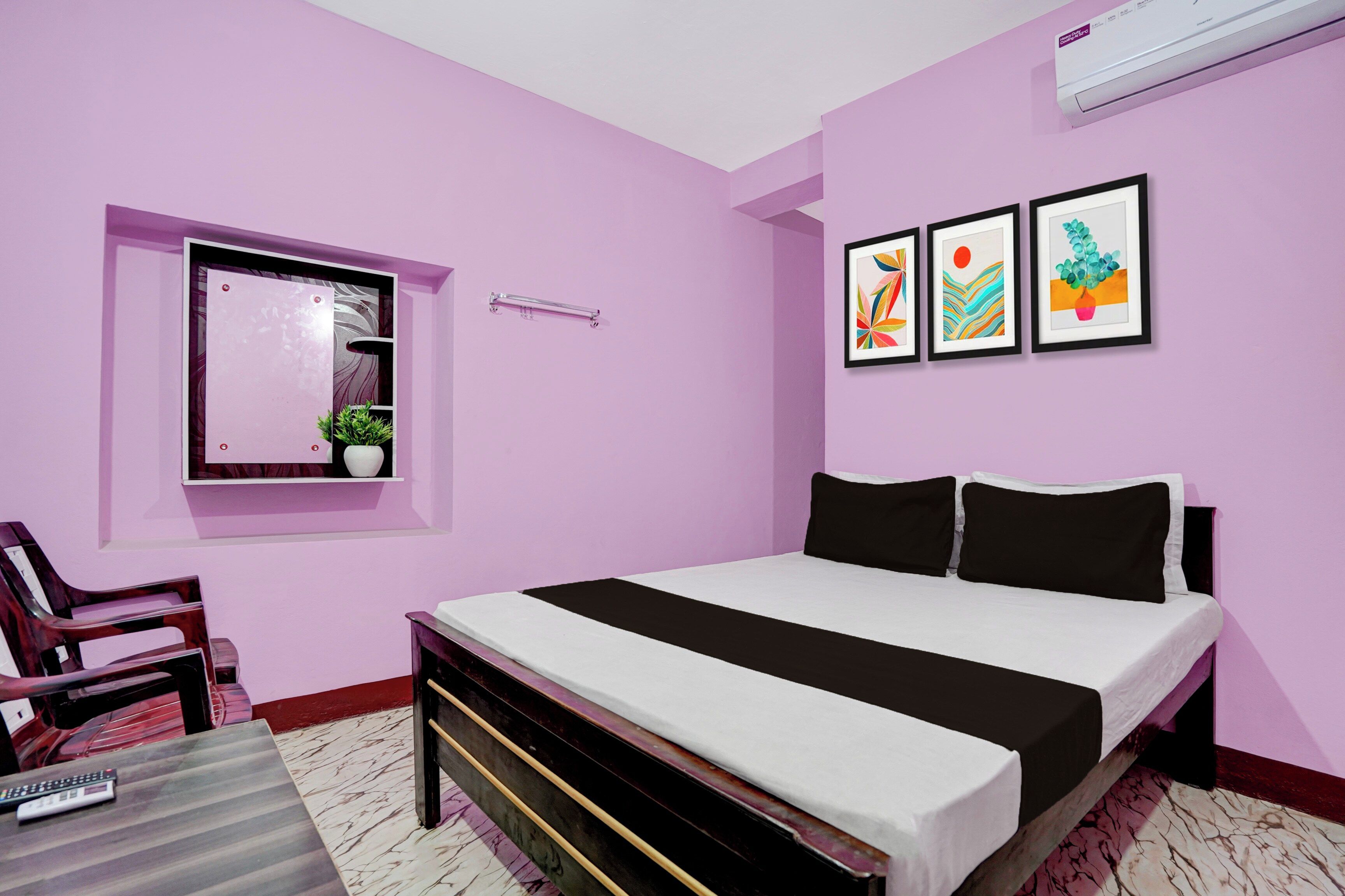 Un dormitorio con cama, una silla, una mesita, una ventana con planta y tres cuadros en la pared.